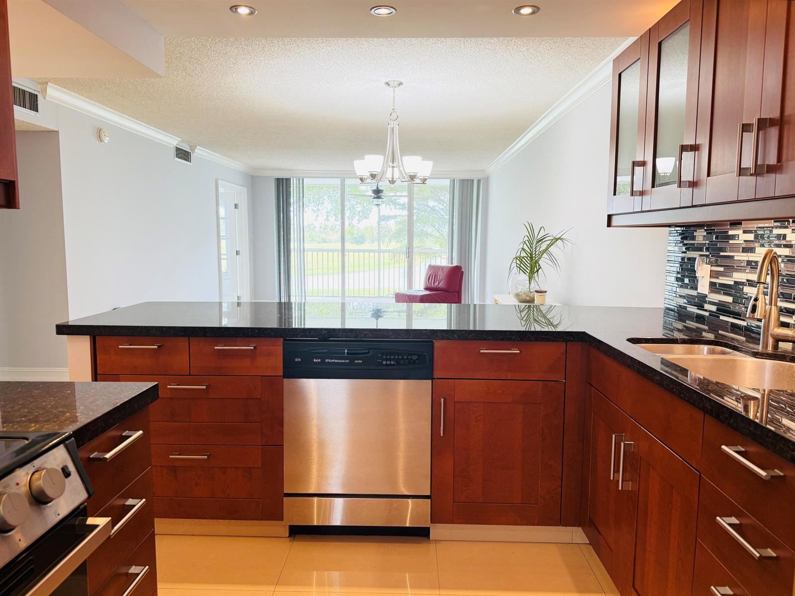 A kitchen with wood cabinets, dark countertops, and a glass door leading to a balcony — 3080 N Course Drive # 202, Pompano Beach FL 33069, POMPANO BEACH, FL