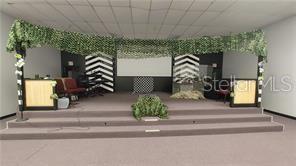 A stage with a carpeted floor, decorative greenery, and chevron-patterned panels in a room — 2921 S ORLANDO DRIVE UNIT 178, SANFORD, FL