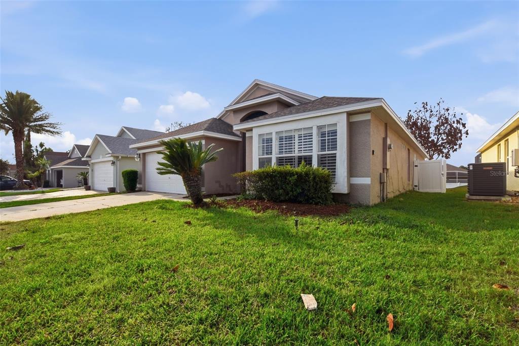 A beige single-story house with a two-car garage and a front lawn under a blue sky — 15833 BAY VISTA DRIVE, CLERMONT, FL