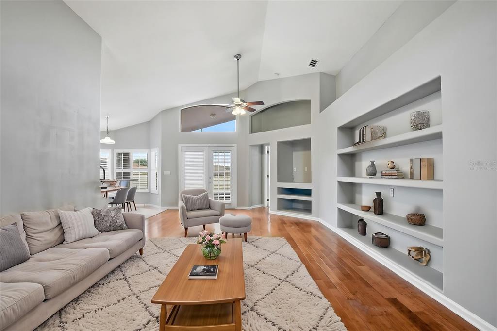 A living room features a vaulted ceiling, hardwood floors, a large rug, and built-in shelving — 15833 BAY VISTA DRIVE, CLERMONT, FL