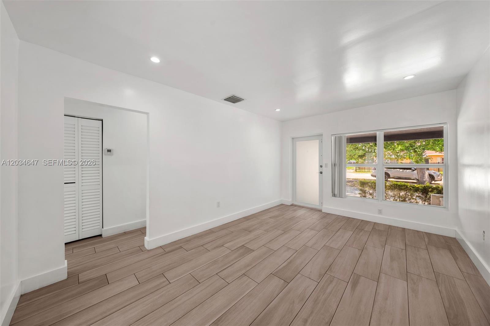 A bright, empty room features white walls, wood-look tile flooring, and a large window — 520 NW 104th St # 520, Miami FL 33150, MIAMI, FL
