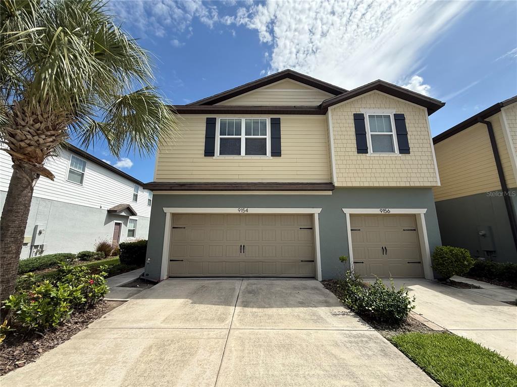 A two-story duplex with tan siding, a shingled upper facade, and two attached garages — 9154 HILLCROFT DRIVE, RIVERVIEW, FL