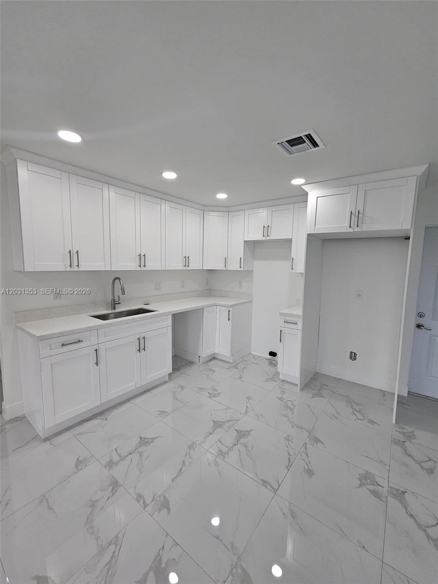 A bright kitchen features white shaker cabinets, marble-patterned tile floors, and quartz countertops — 1901 W 11th Street, Lehigh Acres FL 33971, LEHIGH ACRES, FL