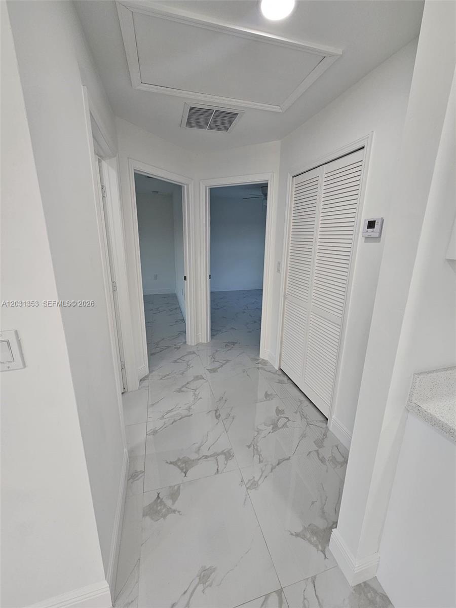 A hallway with white walls, marble-patterned tile flooring, and two doorways leading to rooms — 1901 W 11th Street, Lehigh Acres FL 33971, LEHIGH ACRES, FL