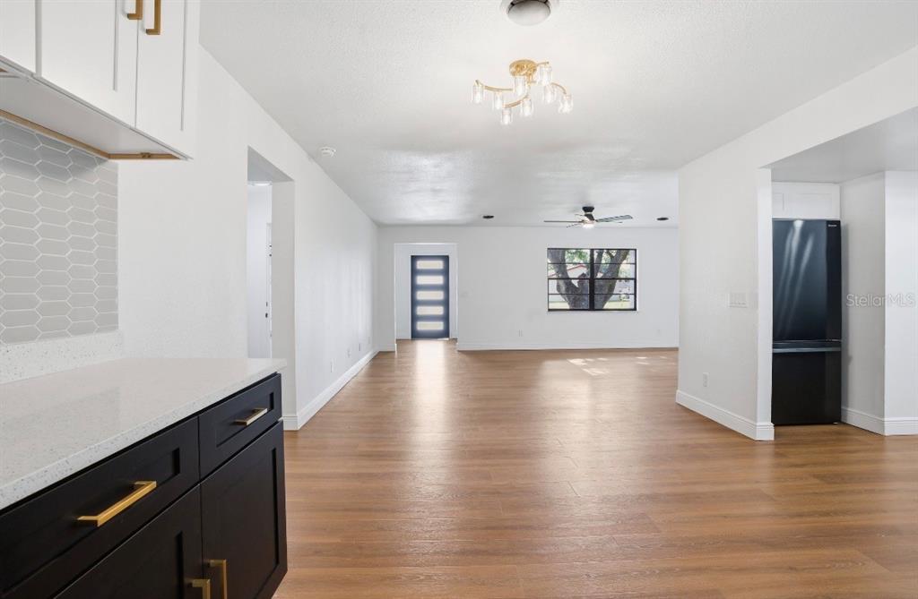 A kitchen with dark cabinets and light countertops opens into a bright living area — 6111 18TH STREET, ZEPHYRHILLS, FL