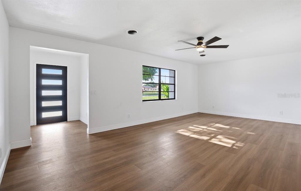 A bright living room features wood-look flooring, white walls, a ceiling fan, and a front door — 6111 18TH STREET, ZEPHYRHILLS, FL