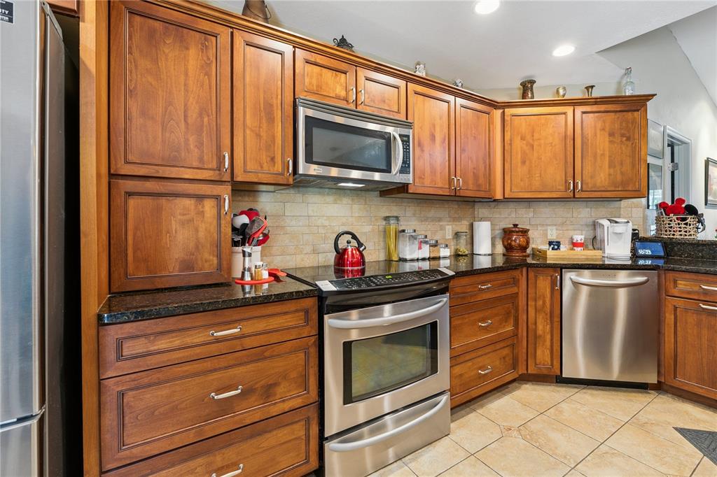 A kitchen features wood cabinets, stainless steel appliances, and a tiled backsplash — 7050 SCENIC HILLS BOULEVARD, LAKELAND, FL