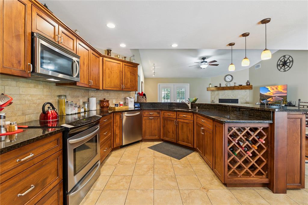 A kitchen features wood cabinets, dark granite countertops, stainless steel appliances, and tile flooring — 7050 SCENIC HILLS BOULEVARD, LAKELAND, FL