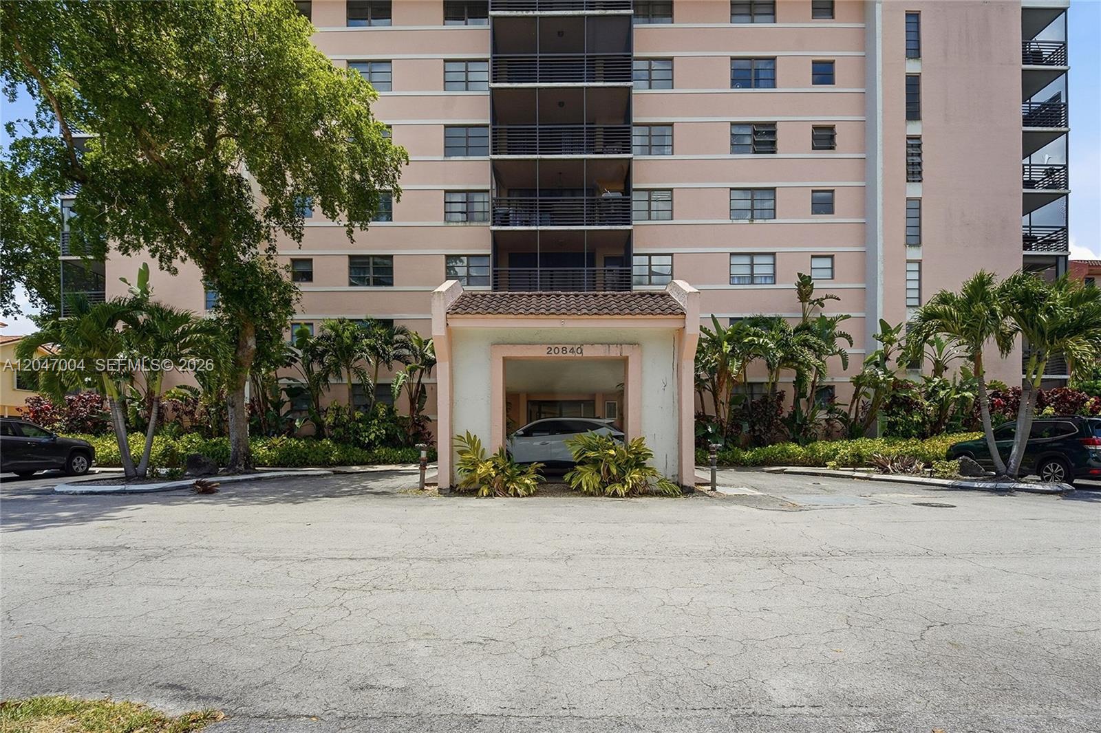 A multi-story pink apartment building features a covered entrance with a car parked underneath — 20840 San Simeon Way # 609, Miami FL 33179, MIAMI, FL