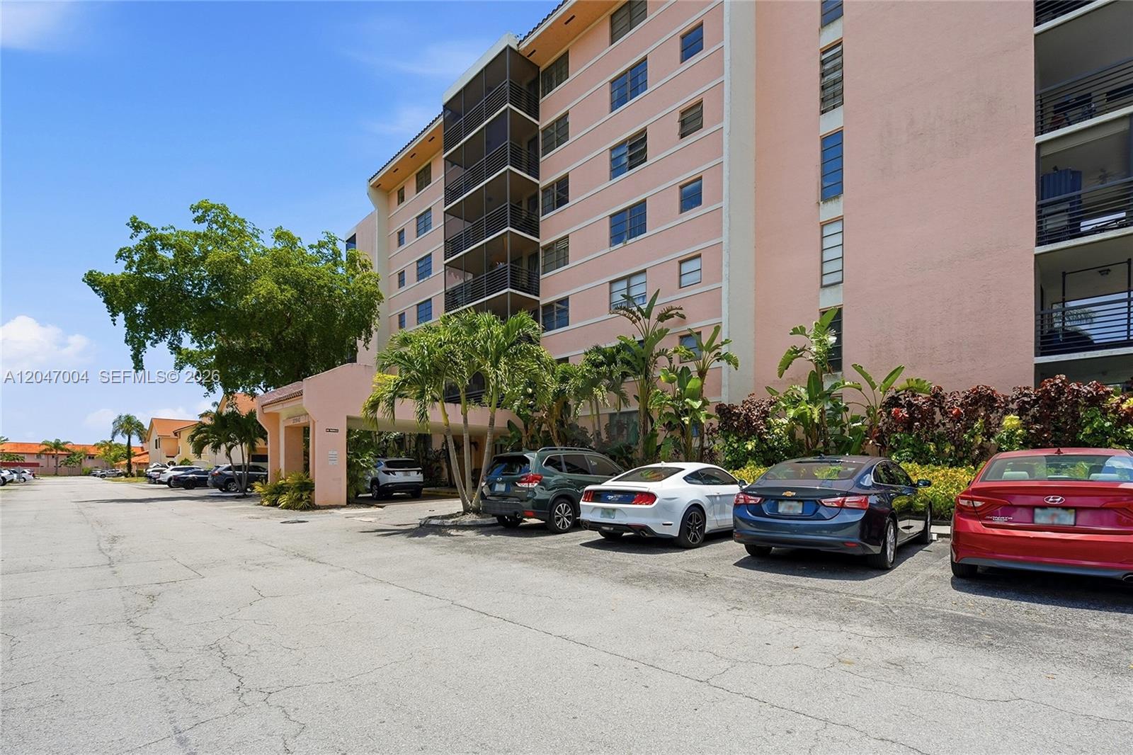 A multi-story pink apartment building features a covered entrance and a parking lot — 20840 San Simeon Way # 609, Miami FL 33179, MIAMI, FL