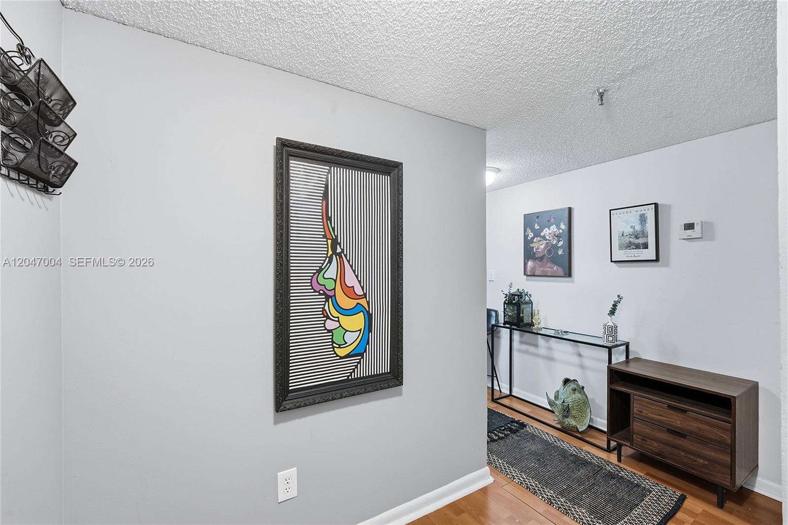A hallway features a colorful abstract face print, a console table, and wood flooring — 20840 San Simeon Way # 609, Miami FL 33179, MIAMI, FL