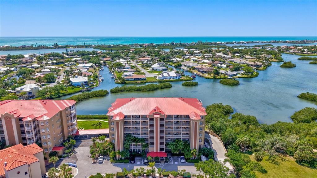 An aerial view shows a multi-story residential building with a red roof near water — 5100 JESSIE HARBOR DRIVE UNIT 304, OSPREY, FL