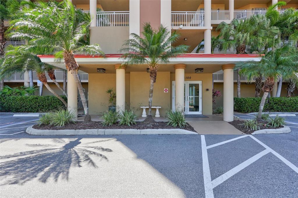 The exterior entrance of a multi-story building features a covered walkway with columns and palms — 5100 JESSIE HARBOR DRIVE UNIT 304, OSPREY, FL