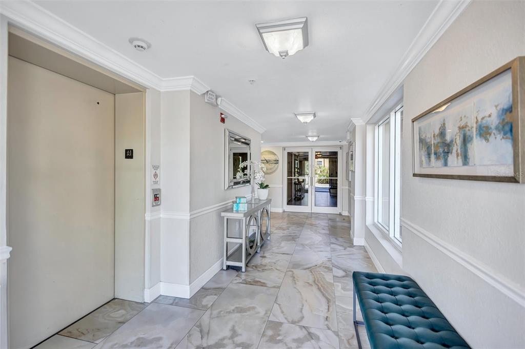 A bright hallway features marble-look tile flooring, an elevator, a console table, and a bench — 5100 JESSIE HARBOR DRIVE UNIT 304, OSPREY, FL