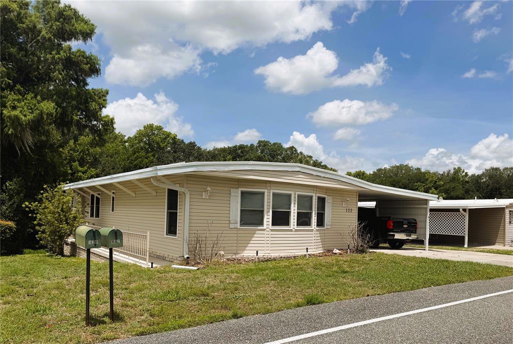 A single-story beige mobile home with a carport and two mailboxes in the front yard — 122 PALO VERDE DRIVE, LEESBURG, FL
