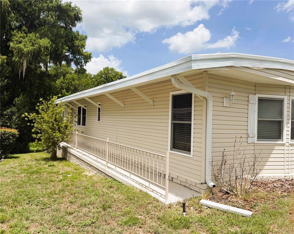 The exterior of a tan mobile home features a long metal railing and a gutter system — 122 PALO VERDE DRIVE, LEESBURG, FL