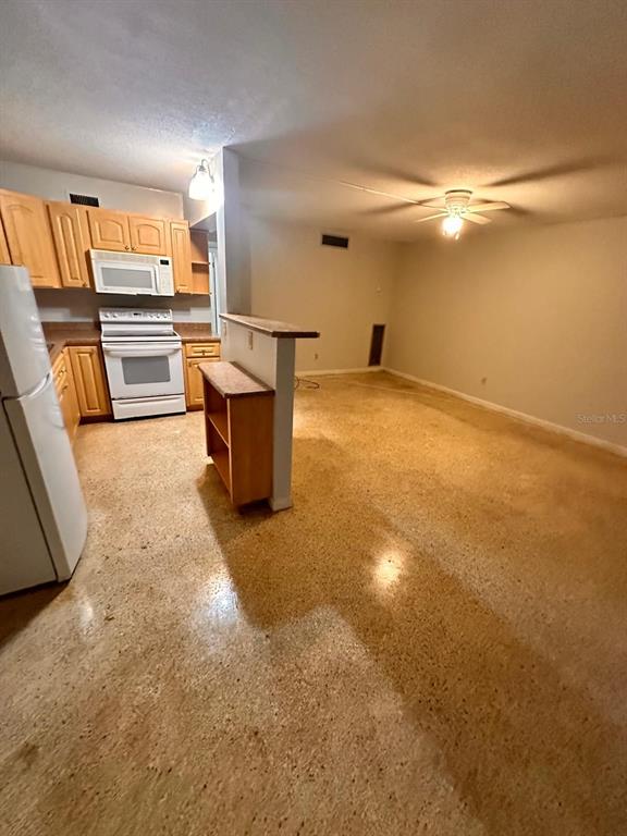 A kitchen with light wood cabinets and a white stove opens into a living area — 305 E DAKIN AVENUE UNIT 11, KISSIMMEE, FL