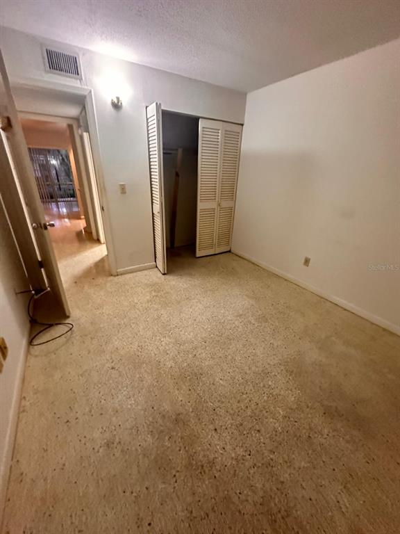 A bedroom with white walls, a louvered-door closet, and speckled flooring — 305 E DAKIN AVENUE UNIT 11, KISSIMMEE, FL