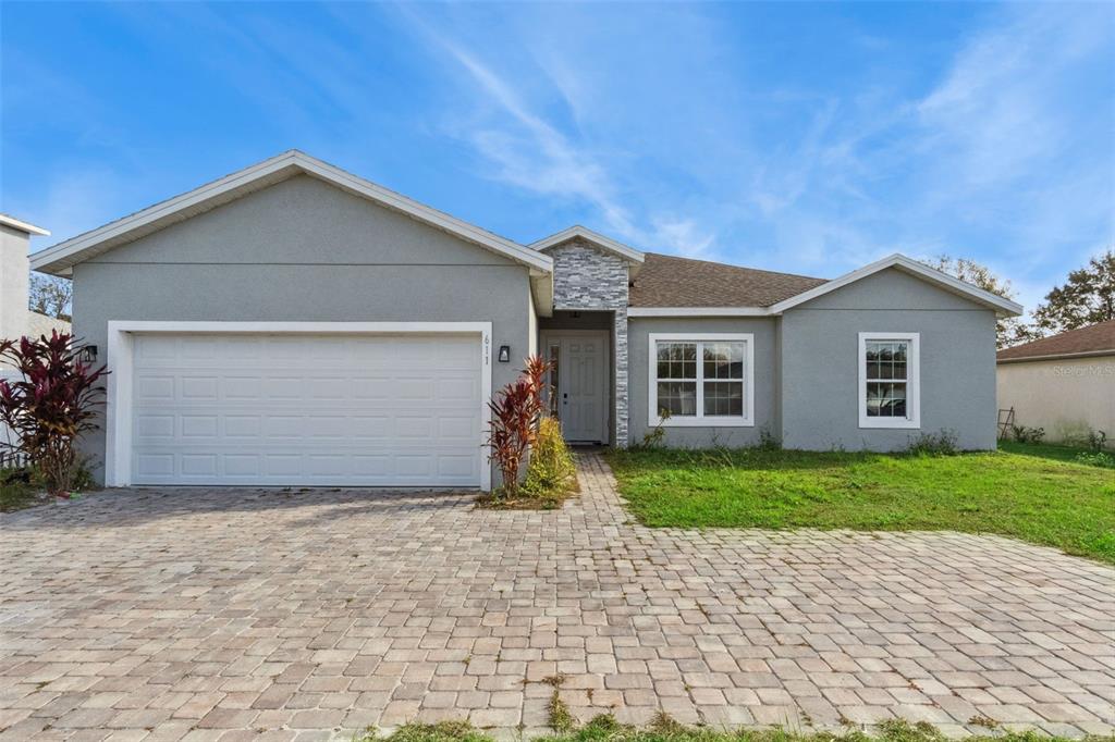 A single-story house with a gray stucco exterior, stone accents, and a paved driveway — 611 GAZELLE DRIVE, POINCIANA, FL