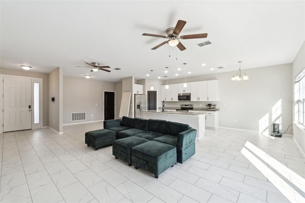 An open-concept living room and kitchen featuring white cabinetry, tile flooring, and a dark sofa — 611 GAZELLE DRIVE, POINCIANA, FL