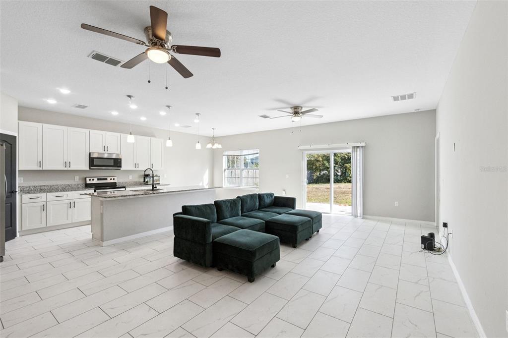 An open-concept kitchen and living area features white cabinetry, granite countertops, and a dark sectional — 611 GAZELLE DRIVE, POINCIANA, FL