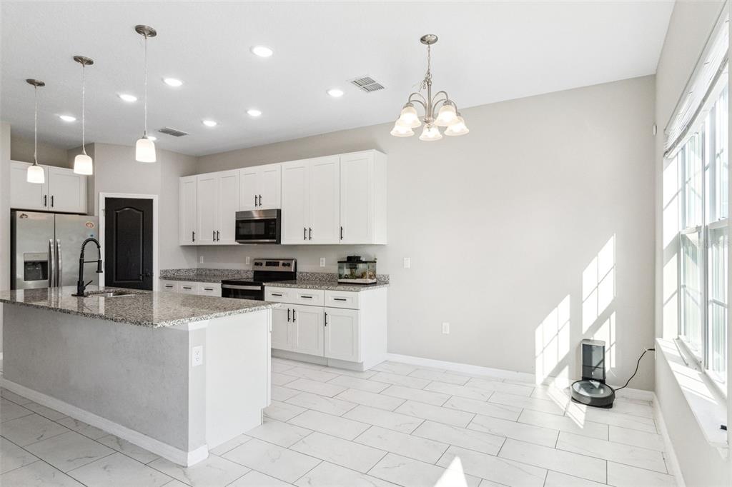 A kitchen with white cabinets, granite countertops, a center island, and tile flooring — 611 GAZELLE DRIVE, POINCIANA, FL