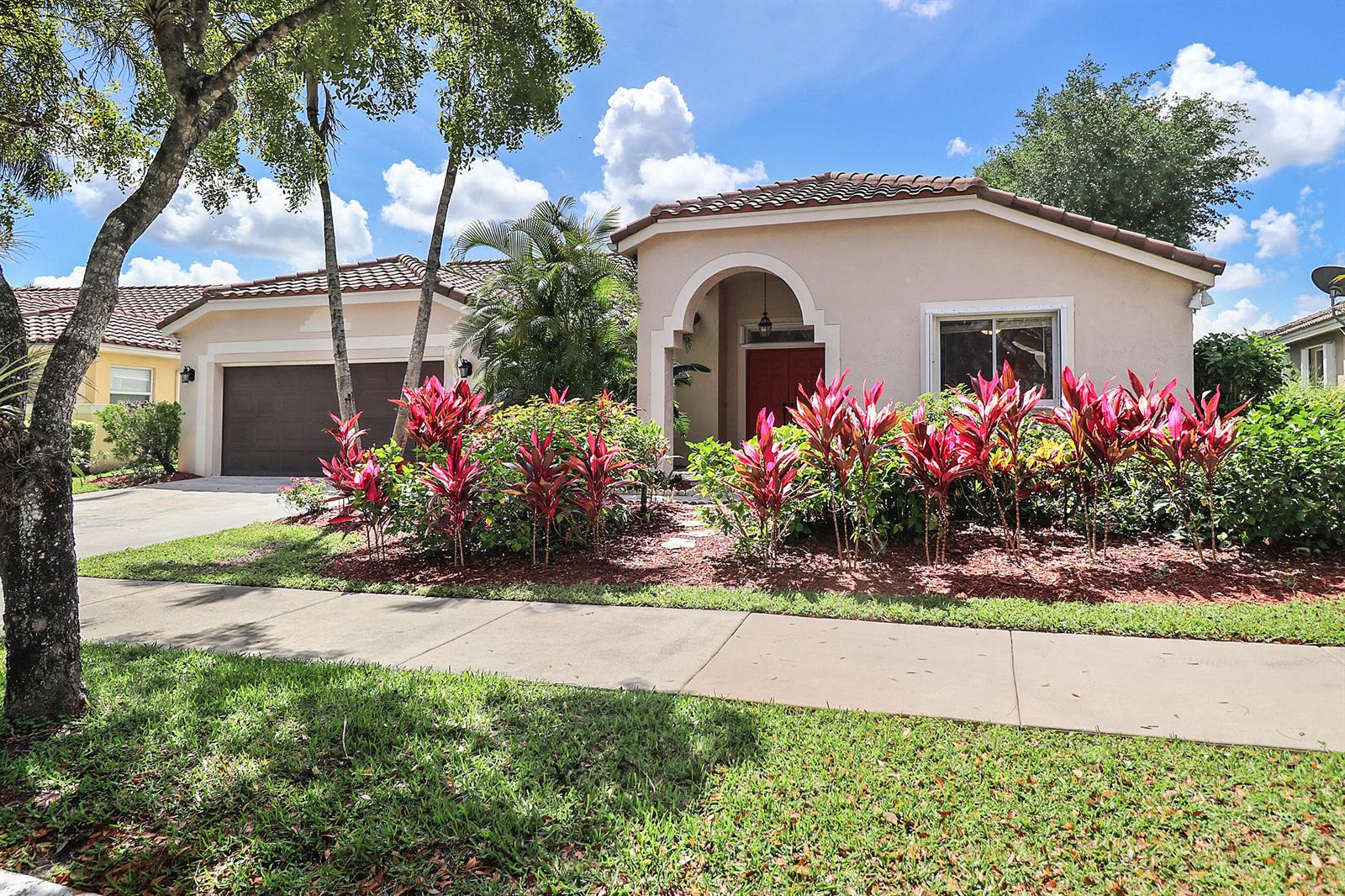 A single-story house with a beige stucco exterior, a red front door, and red-leafed landscaping — 1968 Water Ridge Drive, Weston FL 33326, WESTON, FL