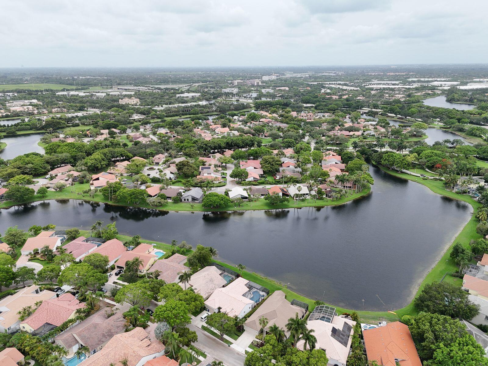 An aerial view shows a suburban neighborhood with houses surrounding a large, central lake — 1968 Water Ridge Drive, Weston FL 33326, WESTON, FL