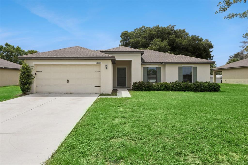 A single-story house with a beige stucco exterior, a two-car garage, and green shutters — 35669 ROSE MOSS AVENUE, LEESBURG, FL