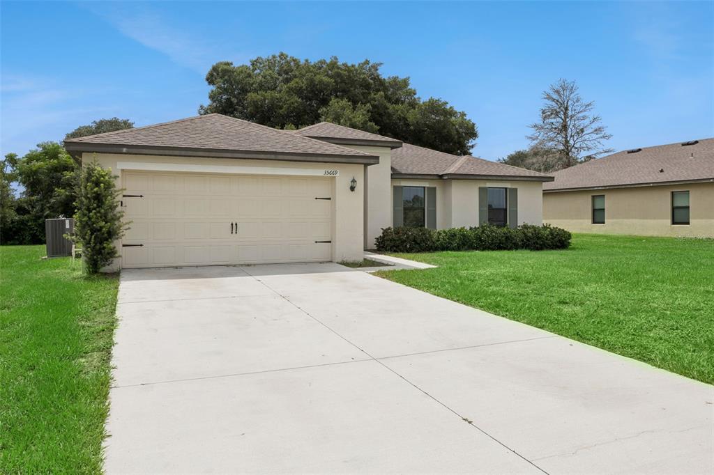 A single-story house with a beige stucco exterior, a two-car garage, and a concrete driveway — 35669 ROSE MOSS AVENUE, LEESBURG, FL