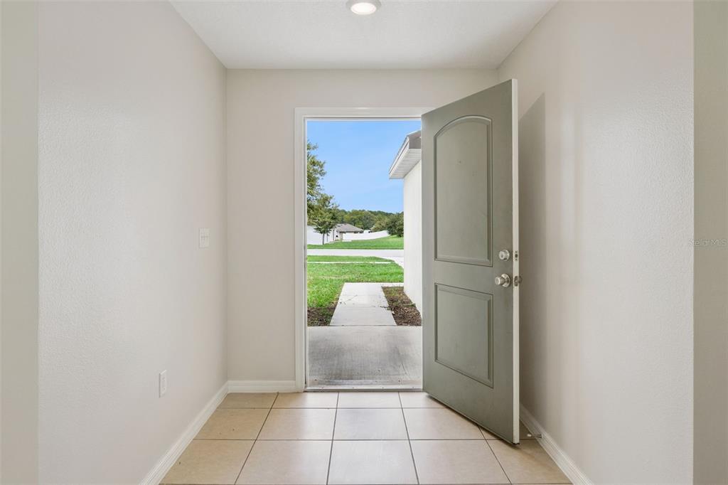 An entryway with light-colored tile flooring and an open door leading to a concrete walkway — 35669 ROSE MOSS AVENUE, LEESBURG, FL