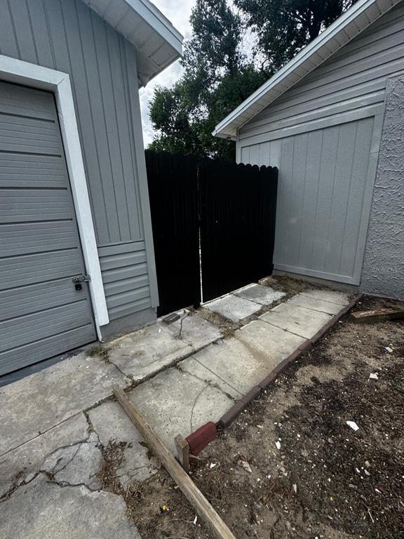 A concrete walkway leads to a black wooden gate between two gray exterior walls — 435 16TH STREET NE, WINTER HAVEN, FL