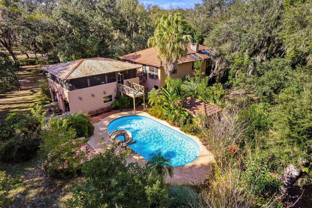 An aerial view shows a two-story house with a pool, slide, and surrounding wooded landscape — 27910 DEBBIE. ROAD, OKAHUMPKA, FL