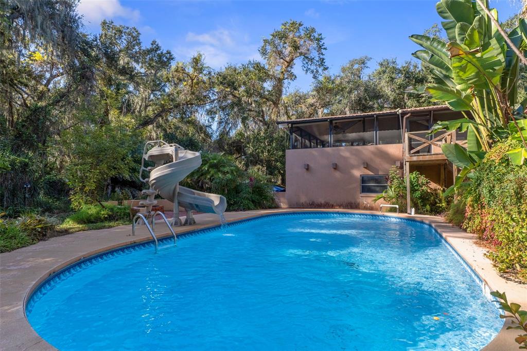 A swimming pool with a spiral slide sits in a backyard next to a house — 27910 DEBBIE. ROAD, OKAHUMPKA, FL