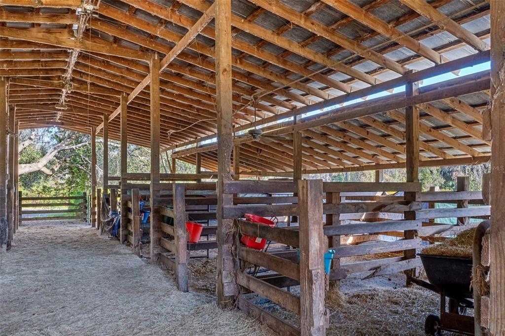 A rustic wooden horse barn with multiple stalls, a dirt floor, and a metal roof — 27910 DEBBIE. ROAD, OKAHUMPKA, FL