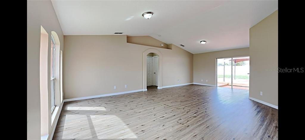 An empty living room with light-colored walls, wood-look flooring, vaulted ceilings, and sliding glass doors — 2436 COURTLAND BOULEVARD, DELTONA, FL