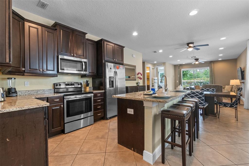 A kitchen with dark wood cabinets, granite countertops, stainless steel appliances, and a breakfast bar — 551 LASSO DRIVE, KISSIMMEE, FL