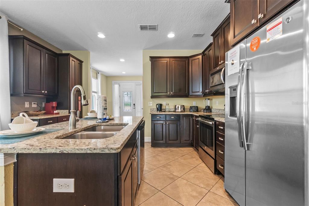 A kitchen with dark wood cabinets, granite countertops, stainless steel appliances, and a central island — 551 LASSO DRIVE, KISSIMMEE, FL