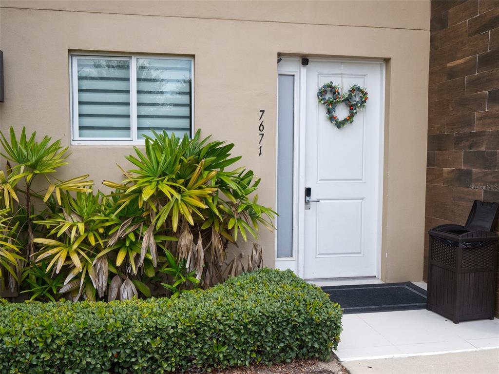 The exterior of a home features a white front door, house numbers, and landscaping — 7671 RECIFE DRIVE UNIT 13-88, KISSIMMEE, FL