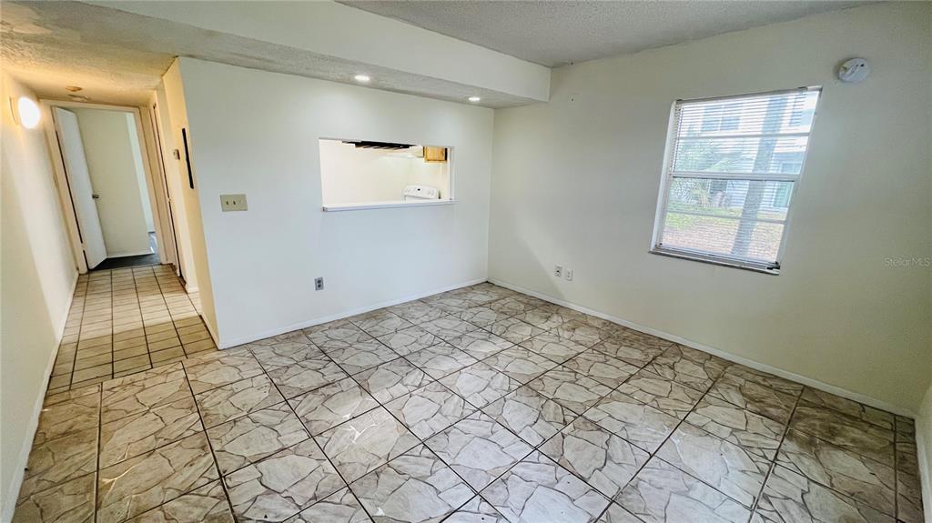An interior view of a room with tiled floors, a pass-through window, and a window — 7120 WATERSIDE DRIVE UNIT 106, TAMPA, FL