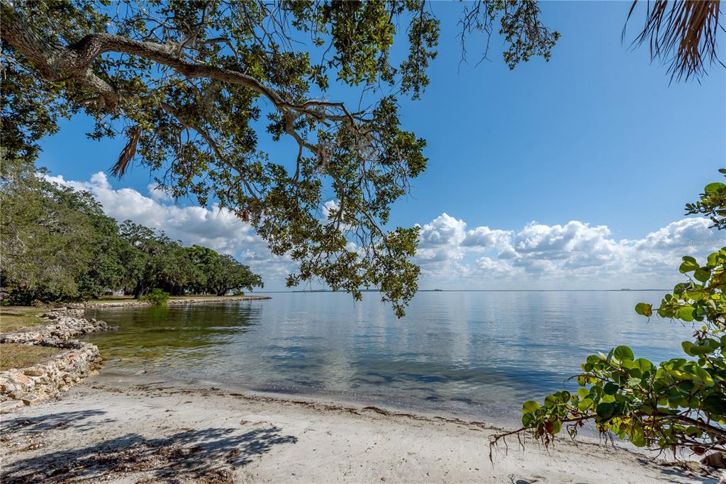 A sandy beach shoreline overlooks a calm bay under a bright blue sky with trees — 6210 BAYSHORE BOULEVARD, TAMPA, FL