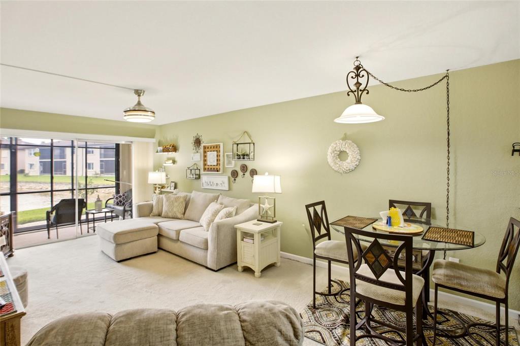 A living and dining area features light green walls, beige carpeting, and a sliding glass door — 25100 SANDHILL BOULEVARD UNIT G103, PUNTA GORDA, FL
