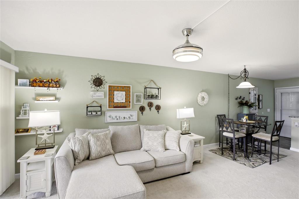 A living room with a light green wall, a sectional sofa, and an adjacent dining area — 25100 SANDHILL BOULEVARD UNIT G103, PUNTA GORDA, FL
