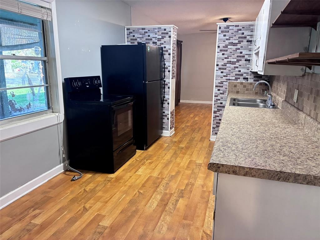 A kitchen features wood-look flooring, black appliances, and a tiled backsplash behind the sink — 120 CLUB ROAD, SANFORD, FL