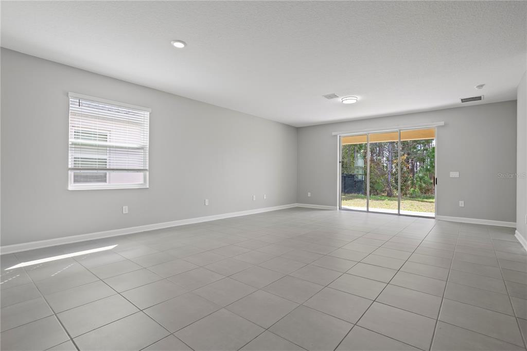 An empty room with light gray walls, large square floor tiles, and sliding glass doors — 3050 CAMDEN WAY, DAVENPORT, FL