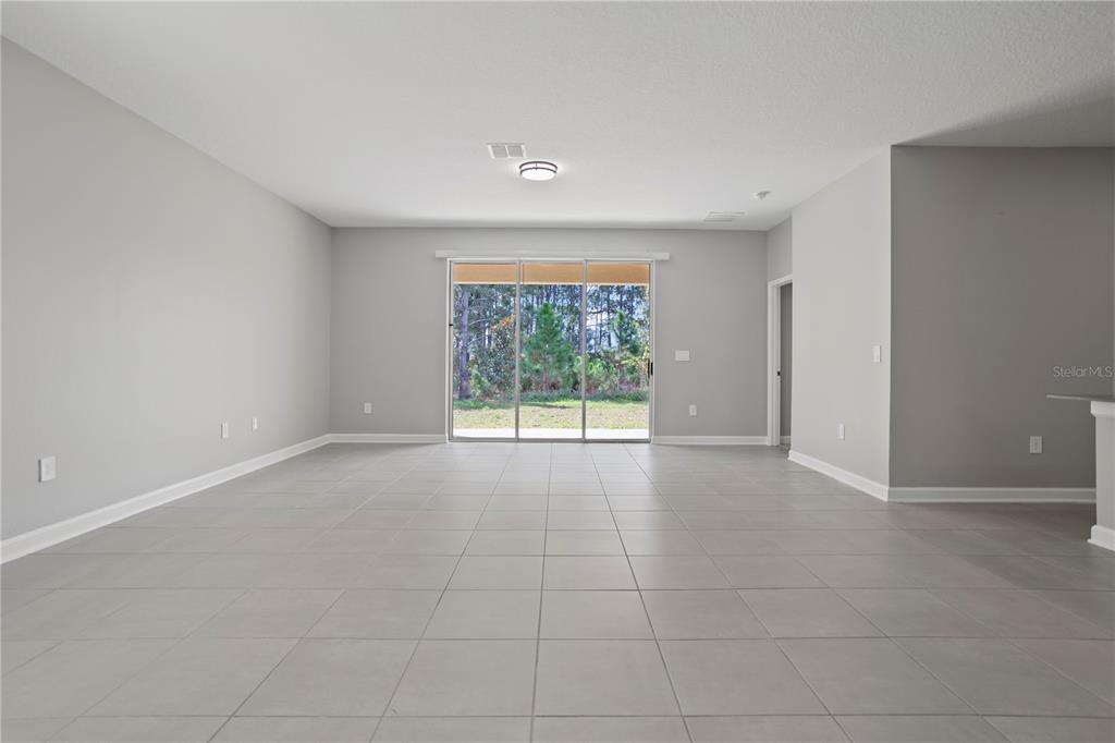 An empty living room features light gray walls, large floor tiles, and sliding glass doors — 3050 CAMDEN WAY, DAVENPORT, FL
