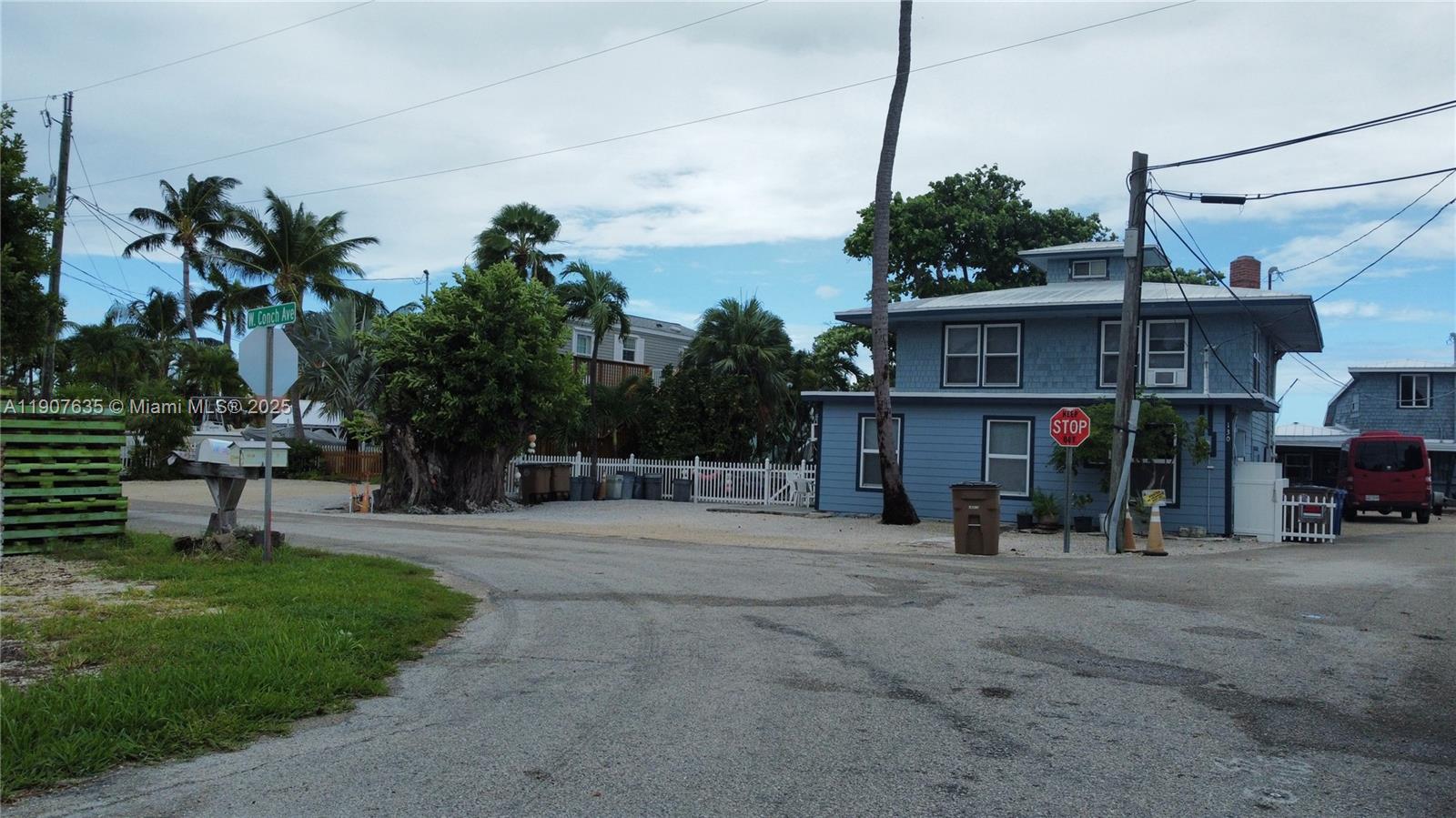 A blue two-story house stands at a street corner with palm trees and a stop sign — 93 N Conch Ave, Marathon FL 33050, MARATHON, FL