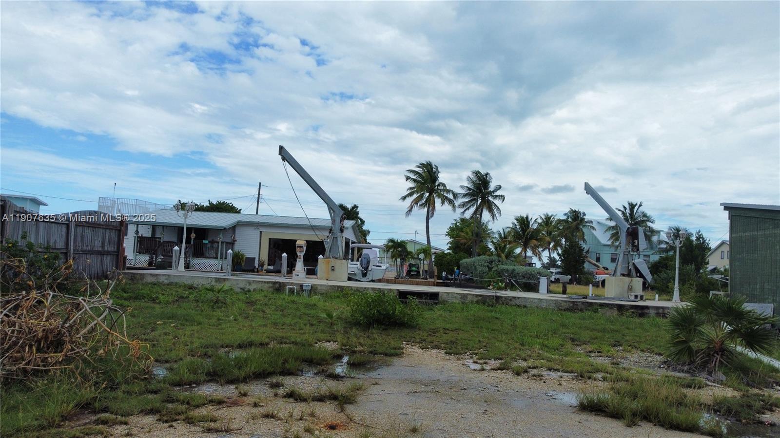 An exterior view shows a grassy lot with two boat lifts and a small house — 93 N Conch Ave, Marathon FL 33050, MARATHON, FL