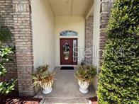 A red front door with an oval glass insert sits beside a brick-faced exterior wall — 231 STRATHMORE CIRCLE, KISSIMMEE, FL