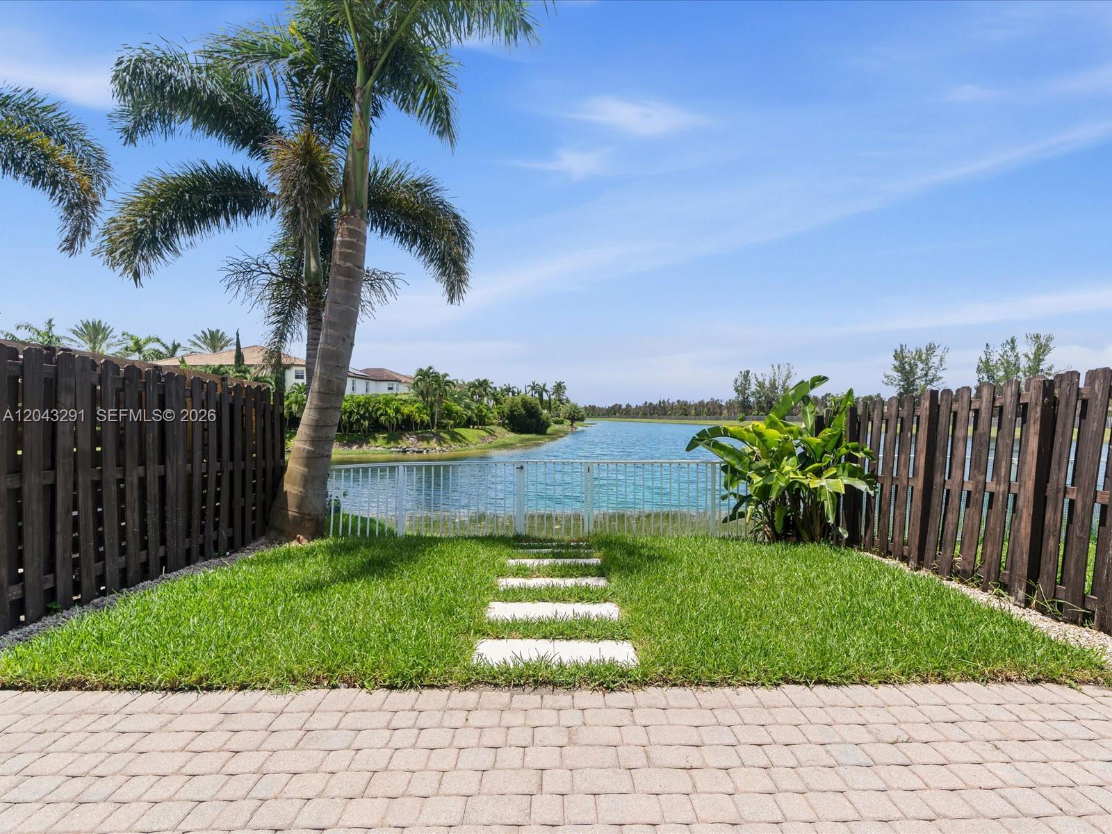 A backyard features a stone path leading to a white gate overlooking a lake — 11628 NW 87th Ln # 11628, Doral FL 33178, DORAL, FL